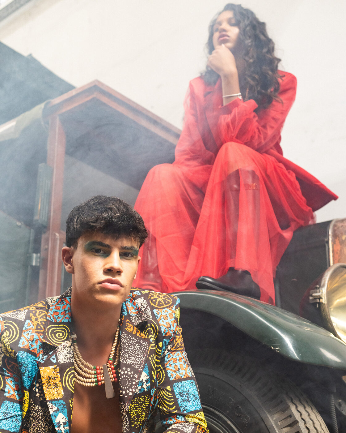 Modelo em blazer estampado com maquilhagem verde; acima, look Flame Scarlet de tule sentado sobre o camião