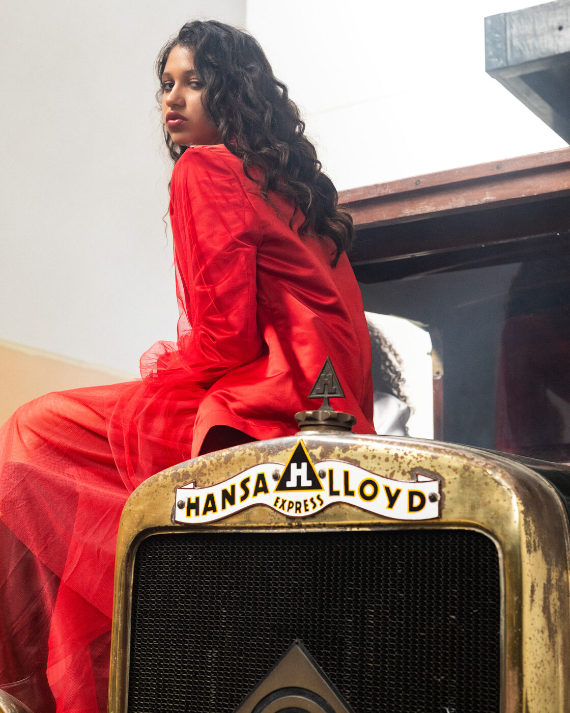 Modelo em look Flame Scarlet de tule sentada sobre a grelha de um camião Hansa-Lloyd
