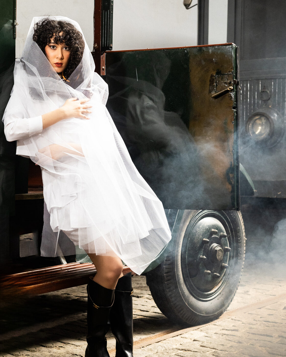 Modelo com véu de tule sobre camisa Bright White e botas altas pretas, no estribo do camião entre fumo