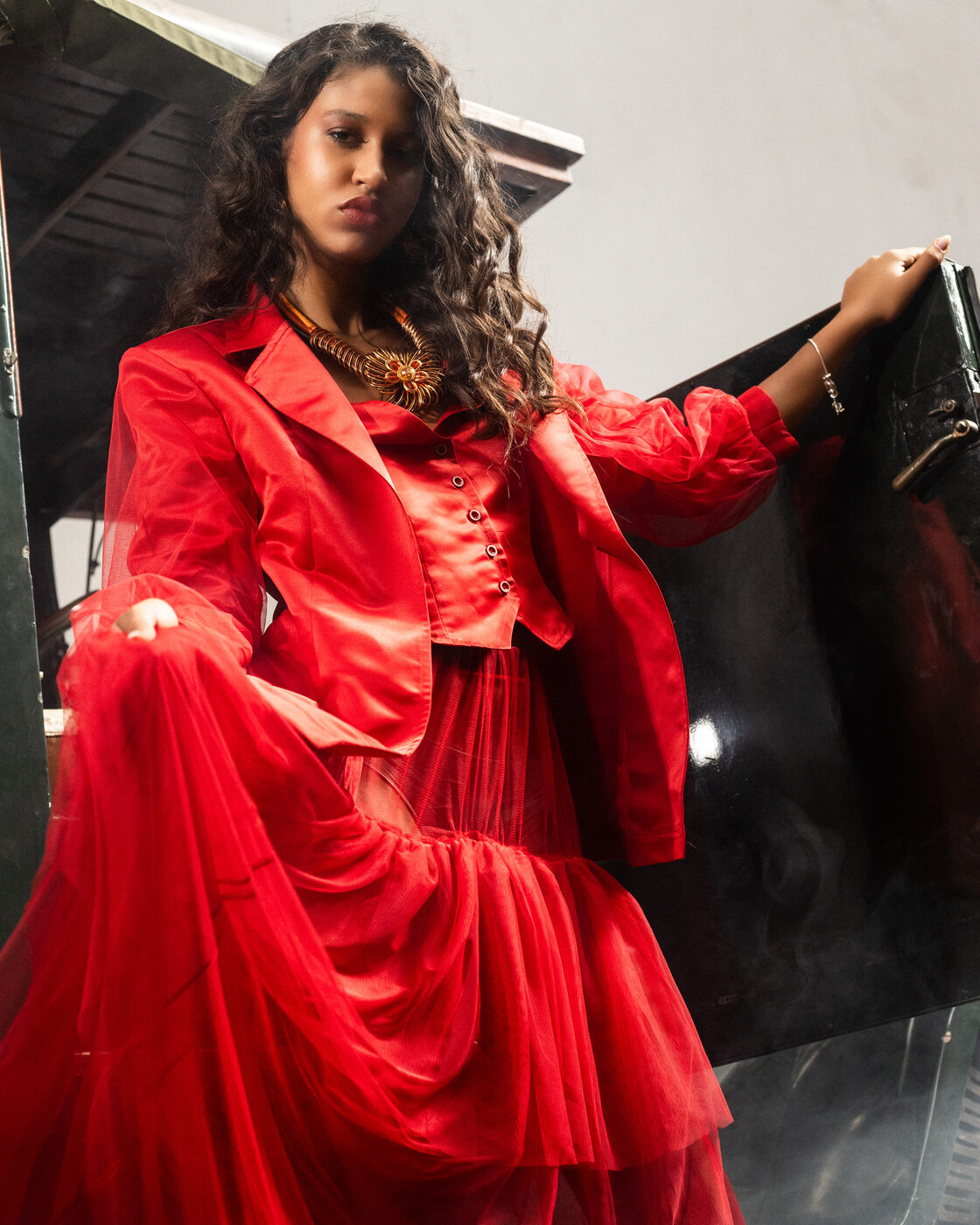 Modelo em casaco de cetim Flame Scarlet, corpete e saia de tule em cascata, nos degraus do camião